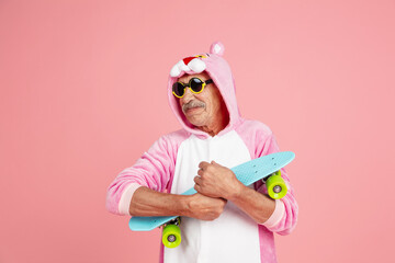 Skater in cool eyewear. Portrait of senior hipster man in stylish attire isolated on pink studio background. Tech and joyful elderly lifestyle concept. Trendy colors, forever youth. Copyspace © master1305