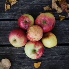 Closeup of a bunch of red apples on a wooden board, surrounded by yellow leaves. Concept of fall, autumn
