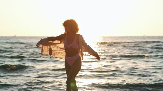 Young african positive optimistic woman in swimwear dancing outdoors on a beach