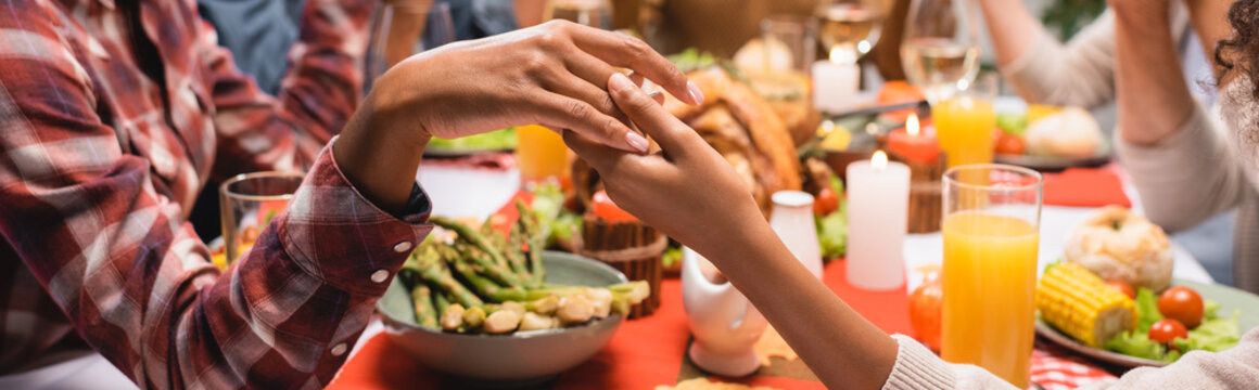 cropped view of african american mother and daughter holding hands while praying during thanksgiving dinner, horizontal image