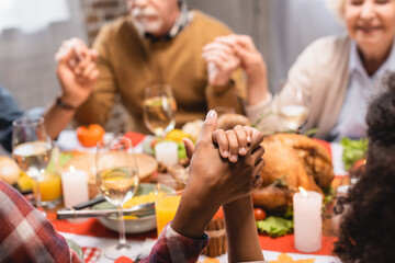 cropped view of multicultural family holding hands while praying during thanksgiving dinner