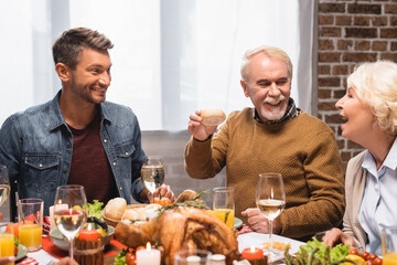 excited man holding bun near wife and son during thanksgiving dinner