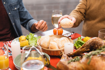 cropped view of senior man holding bun while sitting near son at table with thanksgiving dinner