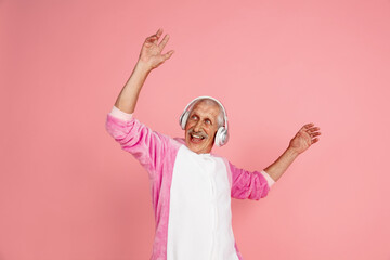Dancing with headphones. Portrait of senior hipster man in stylish attire isolated on pink studio background. Tech and joyful elderly lifestyle concept. Trendy colors, forever youth. Copyspace © master1305