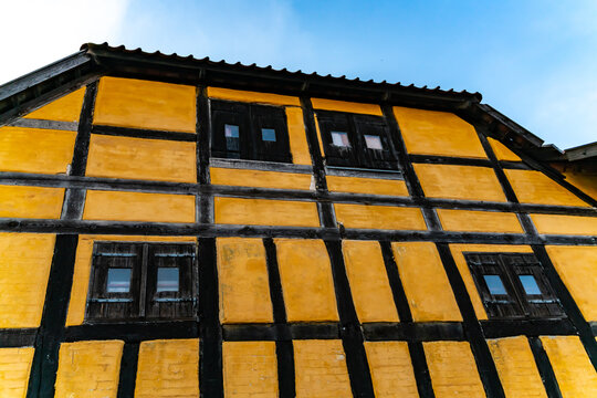 Facade of an old half timbered medieval house in northern Europe, with black wood window shutters and yellow chalk wall.