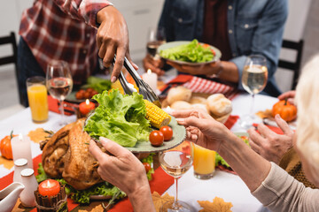 cropped view of senior woman holding plate with vegetables during thanksgiving dinner with multicultural family