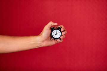 Men holding black alarm clock in one hand on red studio background, copy space.