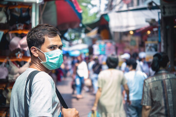 Fototapeta na wymiar Young handsome man walking around market in Thailand with backpack and wearing a face pollution mask to protect himself from the coronavirus.