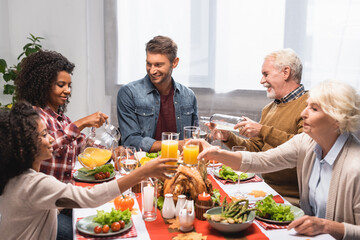 multicultural family clinking glasses with beverages during celebration of thanksgiving day