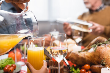 cropped view of african american woman pouring orange juice during thanksgiving dinner