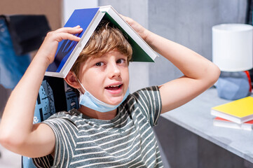 Emotional boy in protective mask rejoices holding a book as a house above his head. Home education....