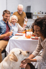 Naklejka premium selective focus of joyful african american girl stroking golden retriever during celebration of thanksgiving day with family