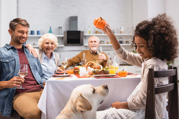 selective focus of african american girl holding decorative pumpkin near golden retriever during thanksgiving dinner with family