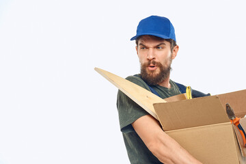 Worker man in uniform with a box in his hands tools delivery service light background