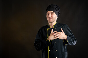 Young male dressed in a black chef suit holds his hands on his chest near his heart