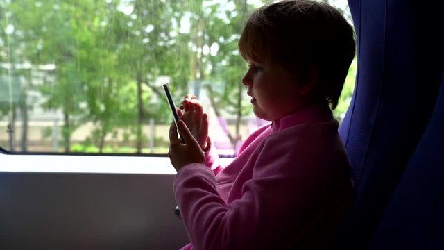 child passenger of suburban train is sitting and using smartphone, playing internet games