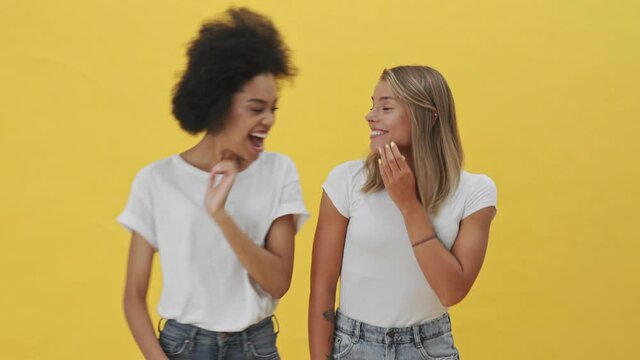 Positive women are sharing secrets standing isolated over a yellow background
