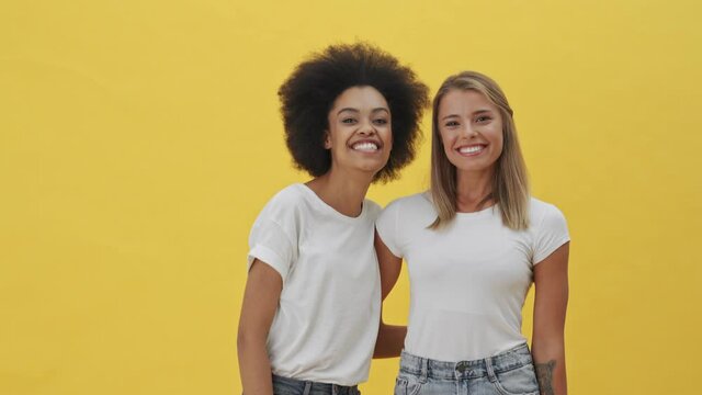 Smiling women are hugging each other standing isolated over a yellow background