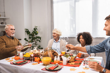 senior man holding bottle of white wine while celebrating thanksgiving with multicultural family
