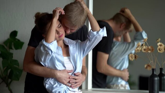 loving couple is hugging each other indoors, standing inside room of apartment, enjoy and caress