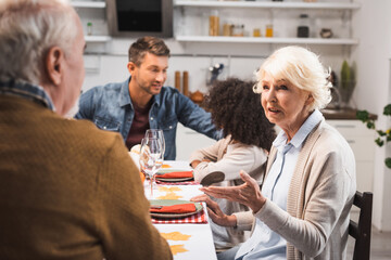 senior woman gesturing while talking during thanksgiving dinner with multicultural family