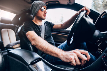 Inside view of a powerful car - a man with stubble in a hat and sunglasses drives confidently...
