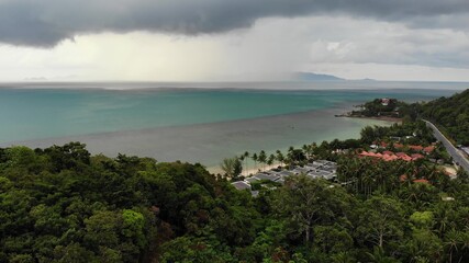 Naklejka premium Overcast sky over tropical island. Gray cloudy sky, green palms on Koh Samui during wet season in Thailand. Drone view. Flying over wild rainforest and jungle near paradise ocean beach. Storm in Asia