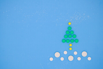 White , yellow and green medical pills in the form of a Christmas tree in the snow on a blue background. Christmas medical flatly.