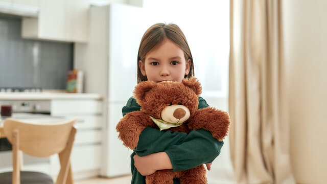 Naklejki A little girl embracing a fluffy brown teddy bear looking into a camera