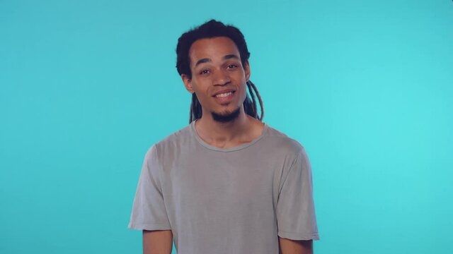 African American man says shh, being speechless, keeps finger on lips, has cheerful expression, asks not to tell secret, isolated over blue background.