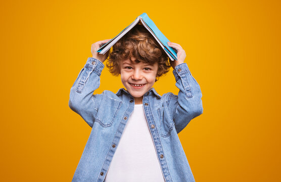 Happy schoolboy hiding under textbook