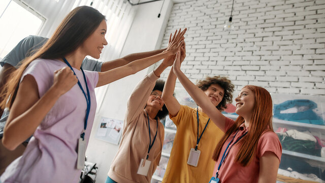 Successful diverse young volunteers celebrating with a high five like a real team while standing in charitable organization office - Powered by Adobe