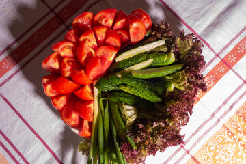Simple summer food - tomatoes, cucumbers, onions, lettuce in a plate on a table with a tablecloth. Vegetarian food.