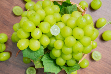 Green grape in Bamboo basket on wooden table in garden, Shine Muscat Grape with leaves in wooden background