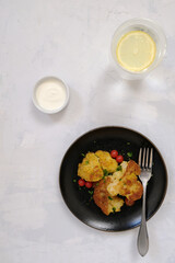 Roasted cauliflower with tomato cherries and fresh parsley on the black plate wuth sour cream and lemon water. Top view
