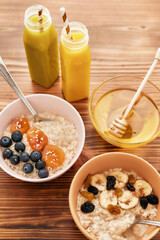 Healthy breakfast ideas, Oatmeal bowl with fresh berries, smoothie in bottles and honey with a dipper on the wooden table