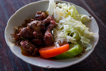 Sate Kambing, is pan-fried of dice cut mutton served in plate with slice tomato, shredded cabbage and lime leaf.