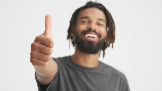 Young african smiling man showing thumbs up gesture isolated over white wall background