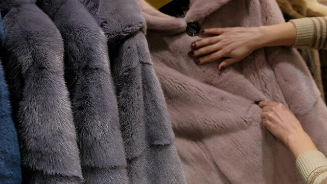 Close up of a woman choosing luxury mink fur winter coat for winter sale on a clothes rack in a retail fashion store.