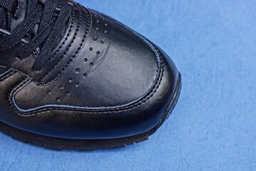 part of one black leather sneaker on a blue background