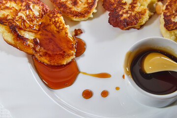 Pancakes on white plate and sweet liquid honey or caramel with a small spoon and with background. Delicious fried flour food. Unhealthy and harmful, but very tasty food.