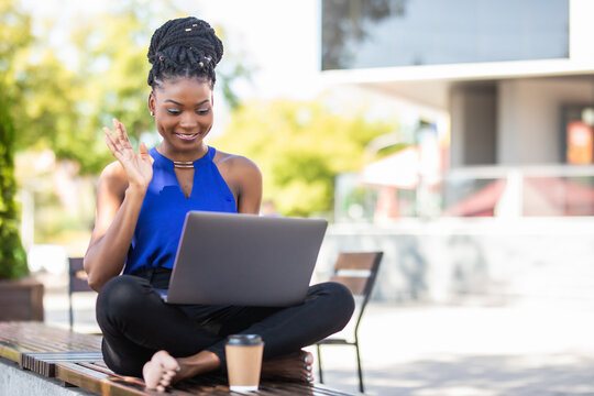 Beautiful young african woman working on laptop computer have video call conversation sitting on a bench outdoors