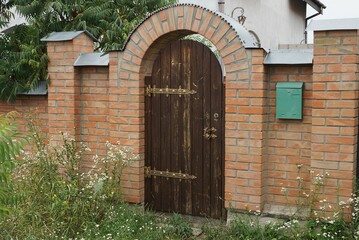 one brown closed wooden door in a brick wall of a fence outside in green grass and vegetation