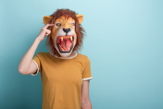 Young woman in lion mask point index finger to the head, isolated on blue background.