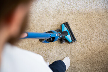 Vacuuming a carpet with a handheld vacuum cleaner, top view.