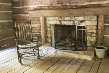 Empty Rocking Char. Empty chair by a fireplace inside a rustic pioneer log cabin. This is a...