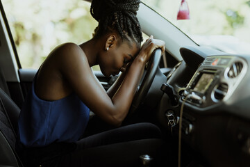 Tired african woman asleep on steering wheel in her car