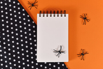 Halloween flat lay with empty notepad and spiders on orange and black background with stars