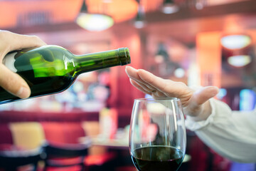 Woman hand rejecting more alcohol from wine bottle in bar