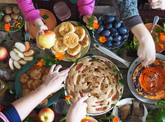 Thanksgiving Day. Festive served table, dishes with fried pumpkin, pies, fruits, berries and vegetables on a wooden background. Hands of guests over the table. Rustic style.